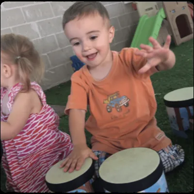 Toddler smiling while playing drums with a friend